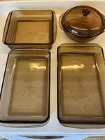 Top-down view of all four dishes showing large rectangular, smaller rectangular, square, and round lidded dishes, smoky brown glass.