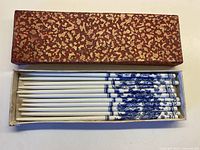 Set of six white ceramic chopsticks with blue dragon design inside original red and gold textured box.