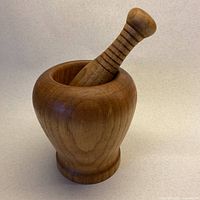 Mortar and pestle set made of solid teak wood with pestle inserted into mortar, showing shape and wood grain.