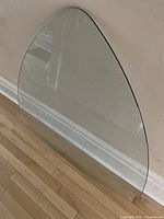 Full view of triangular rounded tempered glass tabletop leaning against a wall showing overall shape and condition.