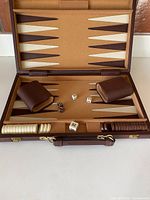 Open vintage backgammon board showing cream and chocolate vinyl playing surface, pieces sorted on side rails, vinyl dice cups and dice on the board.
