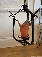 Full view of the vintage wrought iron and brass light fixture suspended off the floor showing the tri-frame design with the orange and grey mottled glass shade installed.