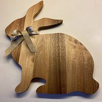 Photo of front side of wooden bunny-shaped cutting board with beige bunny-patterned ribbon tied around the neck.