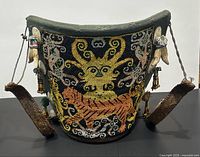 Full front view of cylindrical baby carrier showing beadwork panel with ancestor face and tiger motif