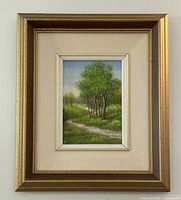 Full view of the framed oil painting with a gold-tone frame and linen mat showing green trees, a dirt path, and sky.