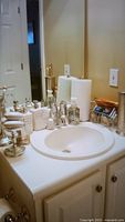 Bathroom sink area showing multiple soap and lotion dispensers, matching soap holder, and other bathroom containers, cream and metallic tones.