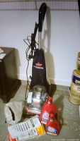 Full view of Bissell steam cleaner with attached PowerBrush and cord wrapped along handle, includes cleaning products and accessory bag on floor.