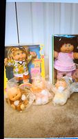 Photo showing five dolls in total with two boxed dolls and three baby Snugglies in plastic bags on floor.