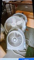 Photo showing three fans: two large white Wind Machine fans and one smaller gray Holmes fan, all showing dust and dirt, placed on the ground in a garage.