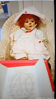 Marie Osmond collectible doll seated in a wicker chair showing full body and certificate in foreground.