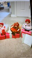 Full view of three Marie Osmond Kissy Tot collectible dolls arranged on the floor with a box and certificate of authenticity visible.
