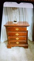 Front view of the solid wood nightstand with four drawers, brass ornate handles, and visible surface scratches on top.