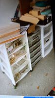 Three stacked plastic storage containers with multiple drawers in a garage. Items stored inside including papers and hand tools.