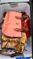 Photo showing peach Kathy Von Zeeland handbag and gold handbag with straps inside a white laundry basket