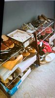 Two stacked wood and wire shoe racks against a gray wall holding multiple pairs of shoes and boots, some boxes visible under racks, shoes mostly size 7.