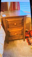 Solid wood side table next to bed, showing front and side view with two drawers and round wooden knobs.