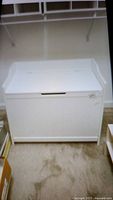 Front view of a white wood storage chest with flat top and recessed handle lid, placed on carpeted floor.