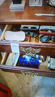 Photo showing multiple sunglasses and eyeglasses in an open wooden drawer with several cases, some branded.