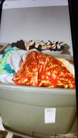 Plastic tote container filled with assorted women's shirts and nightwear, including a prominently visible red and gold patterned silky garment.