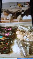 Shelf view of multiple pairs of women's shoes including beige heels, white heels, black patterned flats, cream lace-up flats, and other assorted shoes.