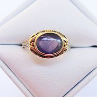 Top‐down view of oval amethyst cabochon set in bezel within geometric gold setting