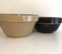 Side view of both antique mixing bowls, wheat-colored one larger on left, chocolate brown on right.