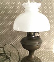 Full view of electrified antique Aladdin oil lamp with white glass chimney and frosted glass shade on dotted cloth background.