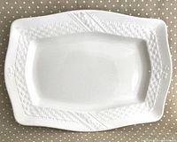 Full view of rectangular white ironstone platter with embossed basket weave border on polka dot fabric background.