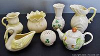 Seven assorted Belleek porcelain pieces showing a creamer jug, vases, flower frog, covered sugar bowl, and swan dish.