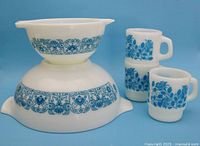 Two Pyrex Blue Horizon nesting mixing bowls stacked, two Anchor Hocking Blue Rose stacking coffee mugs beside them.