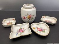 Photo of the covered jar and four trinket dishes showing floral sprays and gold trim on white porcelain, from a front angle.
