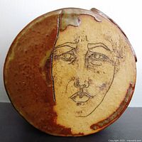 Front view of round pottery vase showing inscribed face design and dual-tone glaze