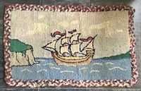 Full view of the rectangular hooked rug with sailing ship design and braided edge on tiled floor.
