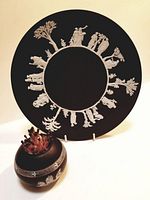 Full shot of both the Wedgwood black basalt plate with classical Greek figures in white relief around edge and round Royal Bayreuth match holder with Corinthian design and striker ridge.
