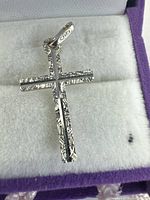Close-up of white gold cross pendant showing detailed textured design and polished finish, visible '750' gold marking on bail.