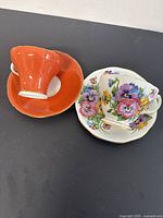 Two bone china teacup and saucer sets; one Queen Anne with pansy floral design and one Aynsley orange with gold trim