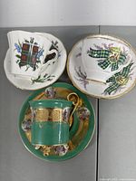 Top view of three distinct bone china teacups and saucers showing colorful tartan and floral designs and green gold ornate cup