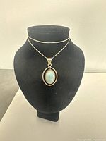 Front view of silver necklace with turquoise pendant displayed on black stand showing overall appearance.