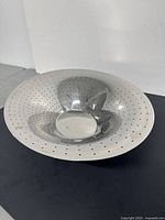 Front angled view of the aluminum perforated bowl showing concave form with multiple small holes and reflective surface.