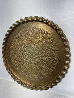 Full view of the round brass tray showing scalloped edges and dense floral etching with central pierced design.