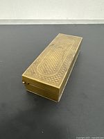 Rectangular ornate brass box showing detailed engraved pattern on top and polished surface.