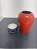 Red ceramic vase with narrow opening next to blue and white Arabia bowl on grey background.