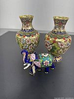 Front view of the two cloisonné enameled vases with floral and gold-tone detailing alongside the colorful elephant figurine in blue, pink, green, and gold accents.