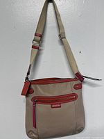 Front view of Coach beige and red crossbody bag with adjustable canvas strap and multiple zippered compartments.