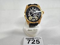 Front view of Guess gold-tone automatic wristwatch on stand, showing black open-heart dial and bezel with minute markers.