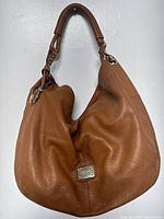 Full front view of brown pebbled leather hobo bag hanging against white wall