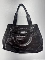 Front view of shiny black patent leather Kate Spade tote bag featuring a prominent bow detail on the front.