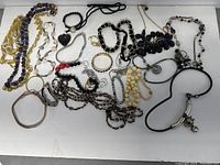 Image showing the full assortment of over 20 costume jewelry pieces including necklaces, bracelets, and rings in various colors and styles laid out on white surface