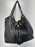 Front view of black pebbled leather Michael Kors shoulder bag with gold-tone hardware, grommets, drawstring closure with tassels