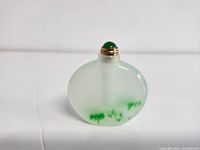 Front view of small iced jade bottle with white and green jade coloration and gold lid topped with green stone